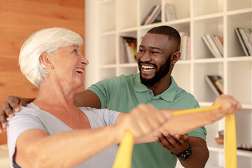 Obraz premium African american male physiotherapist helping senior woman to exercise with resistance bands