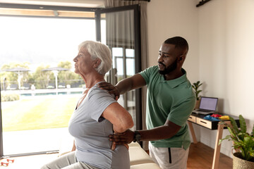 African american male physiotherapist giving back massage therapy to caucasian senior woman at home