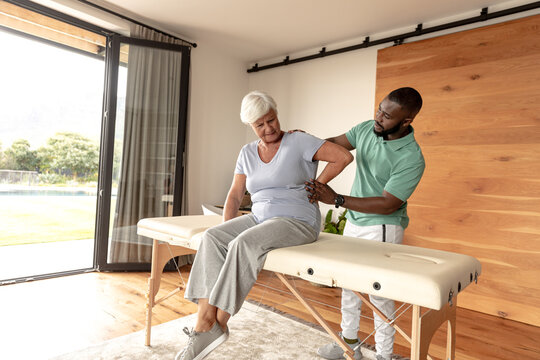 African american male physiotherapist giving back massage therapy to caucasian senior woman at home