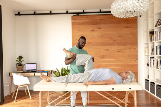 African american male physiotherapist giving leg massage therapy to caucasian senior woman at home