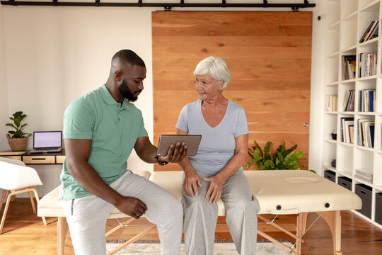 African american male physiotherapist with digital tablet discussing with caucasian senior woman