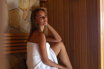 Caucasian young woman in a bathrobe relaxing in the sauna