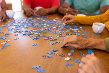 Cropped hands of multiracial seniors arranging jigsaw pieces on wooden table in nursing home