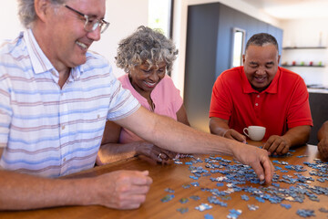 Smiling multiracial senior friends arranging jigsaw pieces on wooden table in retirement home