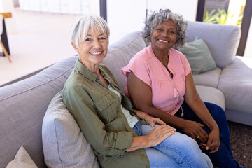 Portrait of smiling multiracial senior female friends sitting on sofa in living room at nursing home - Powered by Adobe