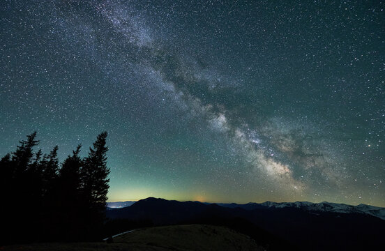 Magical starry night over mountain beskids. Silhouettes of trees, hills and snow-capped mountain peaks under amazing starry sky with Milky way on spring evening.