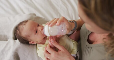Video of happy caucasian mother feeding newborn baby with bottle on bed