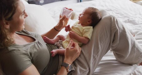 Video of happy caucasian mother feeding newborn baby with bottle on bed