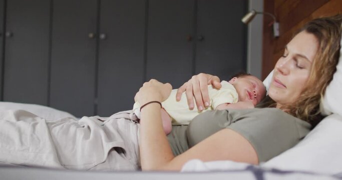 Video of happy caucasian mother sleeping on bed with newborn baby