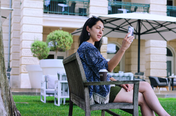 Portrait of young happy business woman relaxing in city, outdoor cafe. Drinking coffee. Using phone. Selfie. technology. Social media. Video call. Summer vacation.