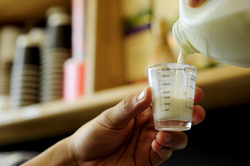 Barista pouring milk to measuring glass for making coffee in a coffee shop