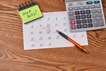 Tax day need help concept. Calculator with calendar and pen. Brown desk background.