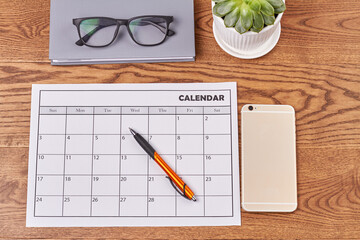 Top view flat lay calendar with smartphone and pen. Book with glasses and pot with plant.