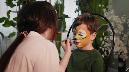 A young woman paints with face painting on the child's face. Children's festival. Face painting, painting with paints on the face of a child