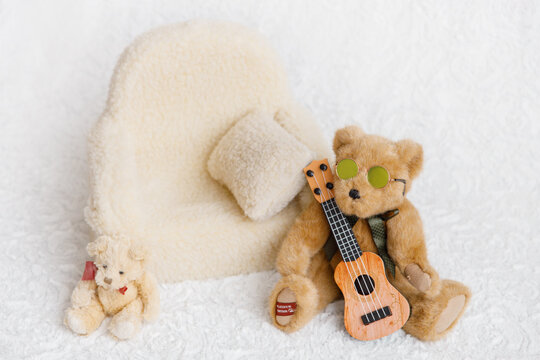 Shoot set up with sofa, teddy bear wearing sunglasses and guitar for newborn on white background. Photo zone for a photo session of newborns. Setup ready for newborn photo shoot and baby photography.