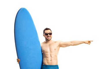 Fit man in swimwear wearing sunglasses holding a surfing board and pointing to the side