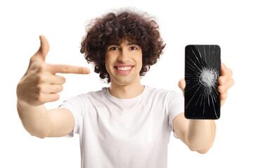 Casual young man with a dark curly hair holding a smartphone with broken screen and pointing