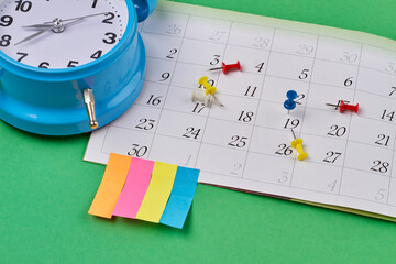 Close-up calendar with push pins and blue alarm clock. Isolated on green background.