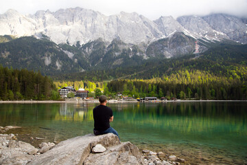 Young man sitting on a stone near the Eibsee Lake, Germany. Travel, lifestyle concept.