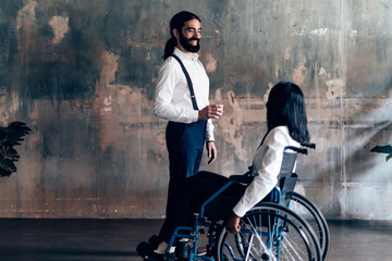 standing elegant gentleman talking to a lady in a wheelchair - two colleagues of different ethnicities speaking together on a work break