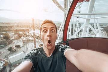 Very excited emotional young man taking selfie photo in cabin of a ferris wheel. Adventures in...