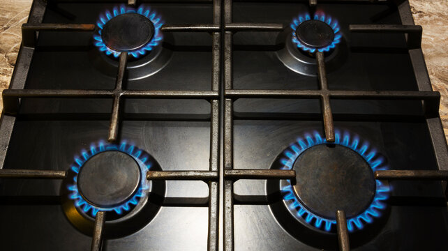 Gas stove with blue tongues of burning gas on four burners