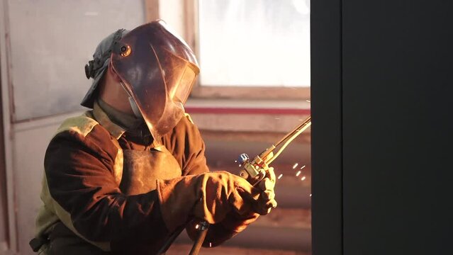 Medium shot . A man (man at the factory)  in a protective mask works with a welding machine.