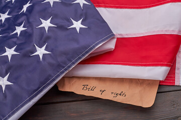 The text bill of rights written on an old piece of paper. Large fabric flag of the United States.