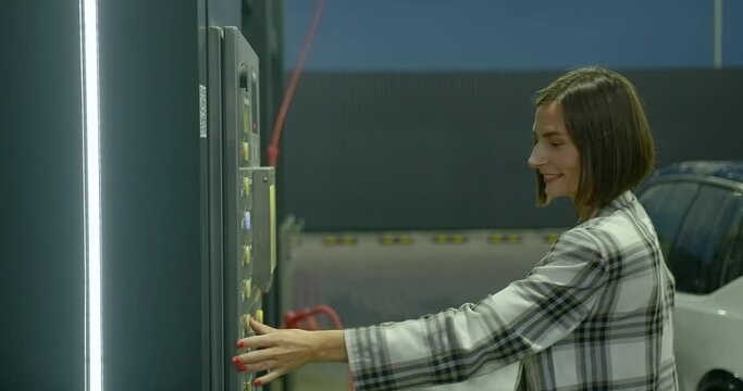 Young woman with a smile presses colored buttons on the car wash