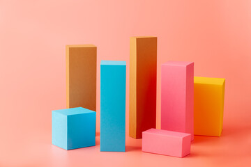 Paper figurines. Rectangles and cubes made of paper or cardboard in yellow, pink, orange and blue. Isolated on a pink background.