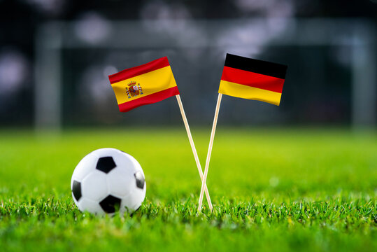Spain vs. Germany, Al Bayt, Football match wallpaper, Handmade national flags and soccer ball on green grass. Football stadium in background. Black edit space.