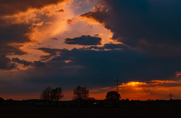 Beautiful sunset with a dramatic sky and overland high voltage lines near Tabertshausen, Bavaria, Germany