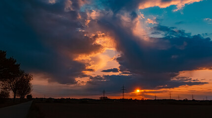Beautiful sunset with a dramatic sky and overland high voltage lines near Tabertshausen, Bavaria, Germany