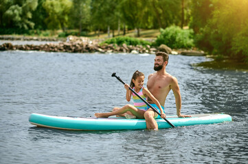 Young man in blue shorts kayaking with his daughter