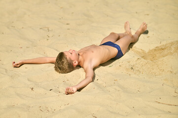 A boy sunbathing while laying on sand and looking relaxed