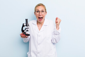 young adult blonde woman feeling shocked,laughing and celebrating success. scientist with a...