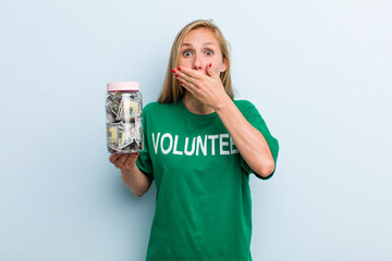 young adult blonde woman covering mouth with hands with a shocked. volunteer and donation concept