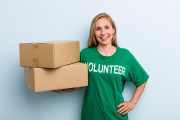 young adult blonde woman smiling happily with a hand on hip and confident. volunteer and donation...