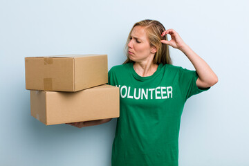 young adult blonde woman smiling happily and daydreaming or doubting. volunteer and donation concept
