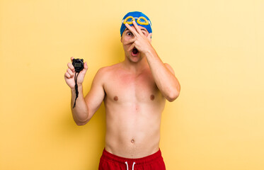 young handsome guy looking shocked, scared or terrified, covering face with hand. swimmer concept
