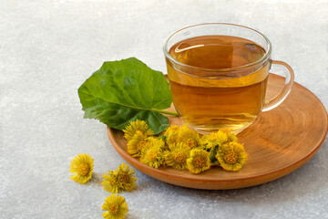 Herbal tea with coltsfoot, flowers and leaves on table