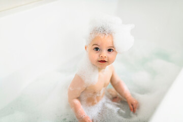 Baby boy bathes in a bath with foam and soap bubbles