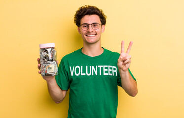 young handsome guy smiling and looking happy, gesturing victory or peace. donation and volunteer...