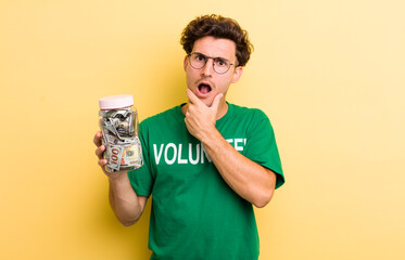 young handsome guy with mouth and eyes wide open and hand on chin. donation and volunteer concept