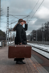 Woman in a dark coat with a suitcase stands on a platform waiting for a train (1308)