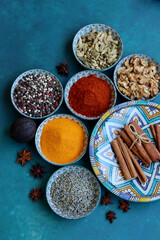 Still life with aromatic spices in ceramic bowls. Peppercorns, turmeric, paprika powder, cinnamon sticks, cardamom, anise and chili pepper close up photo. Blue textured background with copy space.