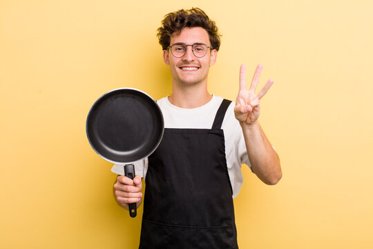 young handsome guy smiling and looking friendly, showing number three. chef with a pan concept