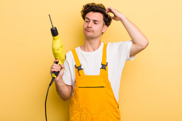 young handsome guy smiling happily and daydreaming or doubting. handyman with a drill concept