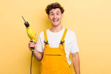 young handsome guy looking happy and pleasantly surprised. handyman with a drill concept
