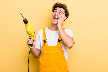 young handsome guy feeling happy, excited and surprised. handyman with a drill concept